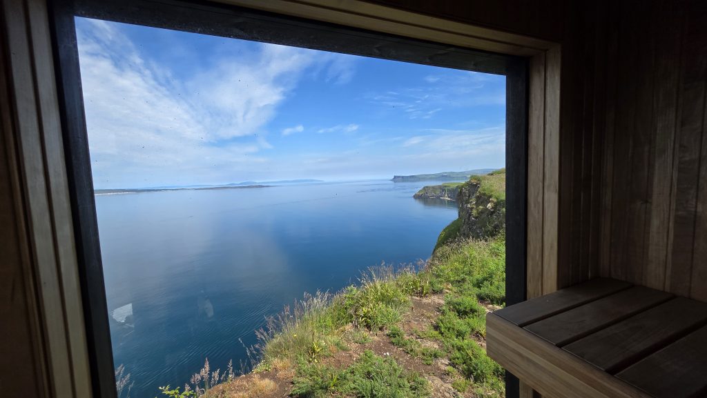 Panoramic Atlantic Ocean and Causeway Coast cliff views through the large window of the coastal sauna at Carrick-a-Rede Retreat
